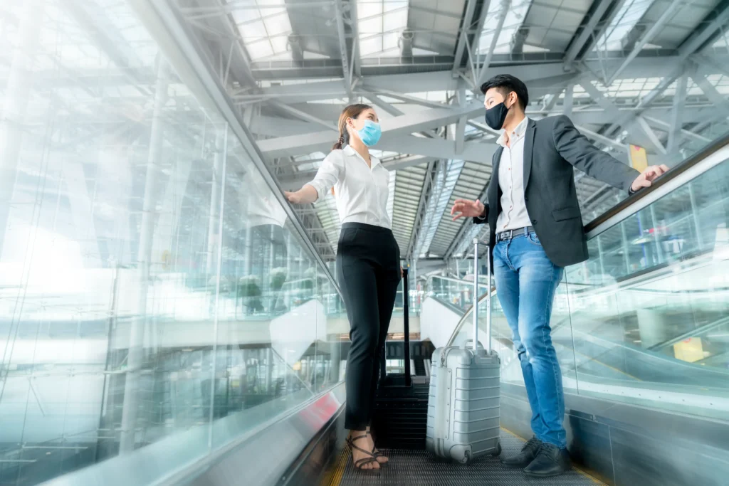 two asian business partners with face mask protection social distancing new normal lifestyle business travellers walking airport with luggage motion movement